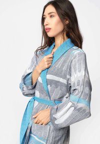 Accappatoio grigio e blu con motivo astratto, tessuto strutturato, colletto a scialle, maniche larghe e cintura in vita. Presenta tasche frontali.