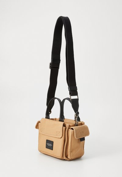 Beige canvas tas met zwarte leren accenten, dubbele handvatten bovenop en een verstelbare zwarte schouderband. Beschikt over twee voorkruiken en een merklabel.