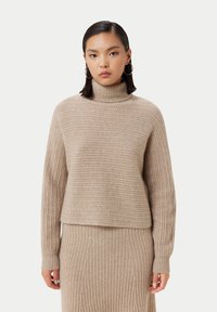 Beige ribbad polotröja med avslappnad passform, som har långa ärmar och en något kortad fåll. Mjukt stickat material genom hela tröjan.