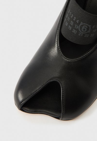 Fekete, nyitott orrú cipő sima bőrből, lekerekített formával és széles elasztikus pánttal a biztos illeszkedésért. Látható fém részek vagy minták nélkül.