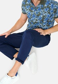 Kortärmad polo med grön bas och blå tropisk blommönster, kombinerad med marinblå chinos och vita sneakers.