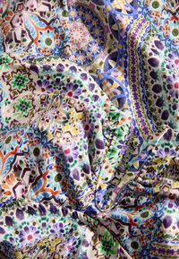 Mehrfarbiger Stoff mit komplexen floralen und geometrischen Mustern; zeigt wirbelnde Formen in Lila, Grün und Orange auf einem hellen Hintergrund.