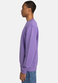 Purple sweatshirt with long sleeves, ribbed cuffs and hem, featuring a simple design and a soft texture. Worn over denim jeans.