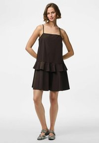 Vestido marrón con un corsé ajustado, tirantes finos y un dobladillo con volantes en capas. Combinado con zapatos a rayas en blanco y negro.