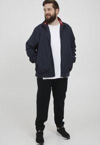Jachetă bomber ușoară de culoare bleumarin cu accente roșii și albe la guler, asortată cu pantaloni negri și adidași negri, având o croială relaxată.