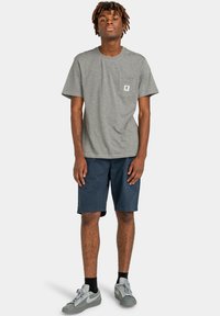 T-shirt en coton gris avec une poche poitrine, associée à un short marine et des baskets grises. Style décontracté, coupe relax avec des manches courtes.