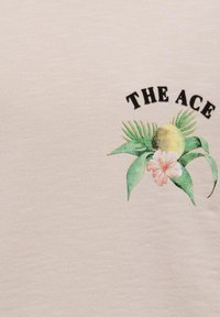 Tela beige claro con un gráfico colorido que presenta hojas de palma, una fruta amarilla y una flor rosa, acompañada del texto "THE ACE."