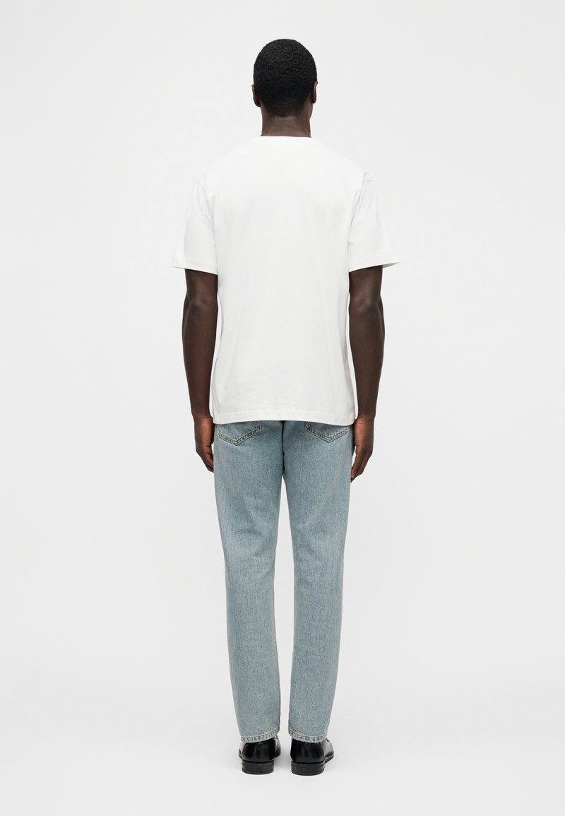 Weißes Baumwoll-T-Shirt, kurze Ärmel, lockere Passform, kombiniert mit hellblauen Jeans. Schlichtes Design, Standard-Rückenansicht, keine sichtbaren Muster oder Akzente.