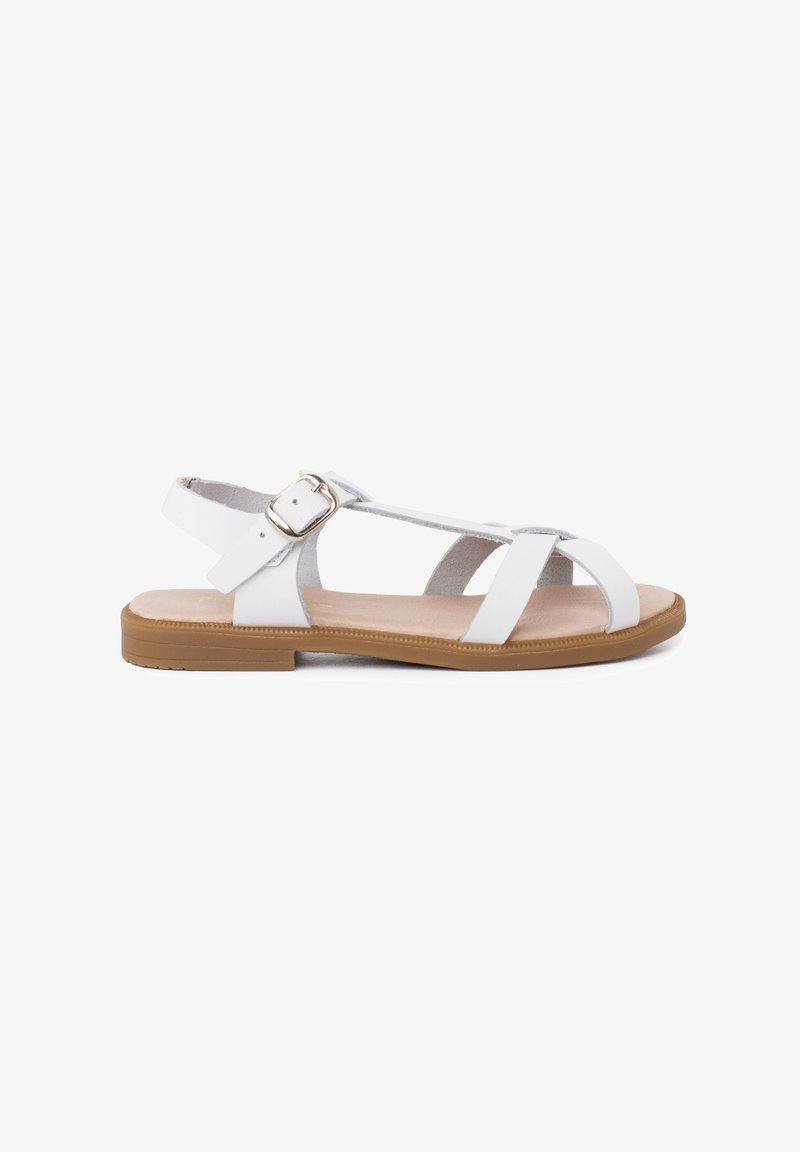 White leather sandals with a flat sole, featuring crisscross straps and a side buckle for adjustability. Tan outsole for contrast.