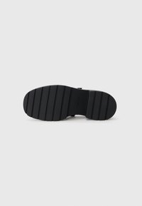 Suola in gomma nera con texture orizzontale e scanalature, caratterizzata da una leggera curvatura all'estremità, etichettata con "Calvin Klein" vicino al tallone.
