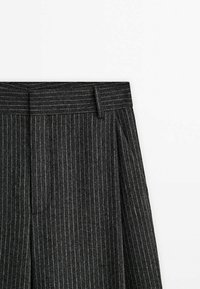 Pantalon ajusté gris foncé à fines rayures avec passants de ceinture et pli marqué à l'avant sur fond blanc uni.