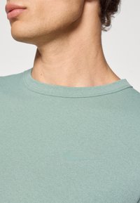 Camiseta Nike verde menta con cuello redondo. Presenta un logo Nike sutil y tonal en el pecho. Textura de tela suave y lisa.