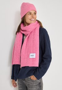 Rosa gestrickter Schal mit einem Fischgrätenmuster, präsentiert mit einer passenden Mütze. Der Schal verfügt über ein Markenlabel und ist aus weichem Material gefertigt.