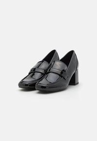 Mocassins à talons carrés en cuir verni noir et brillant avec une large bande sur le vamp et un orteil arrondi. Texture lisse, design de talon empilé.