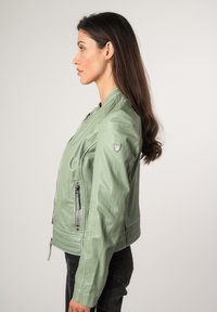 Giacca da moto in pelle verde chiaro con tasche con cerniera, dettagli a coste e design aderente. La vista laterale mette in evidenza la sua forma slanciata.