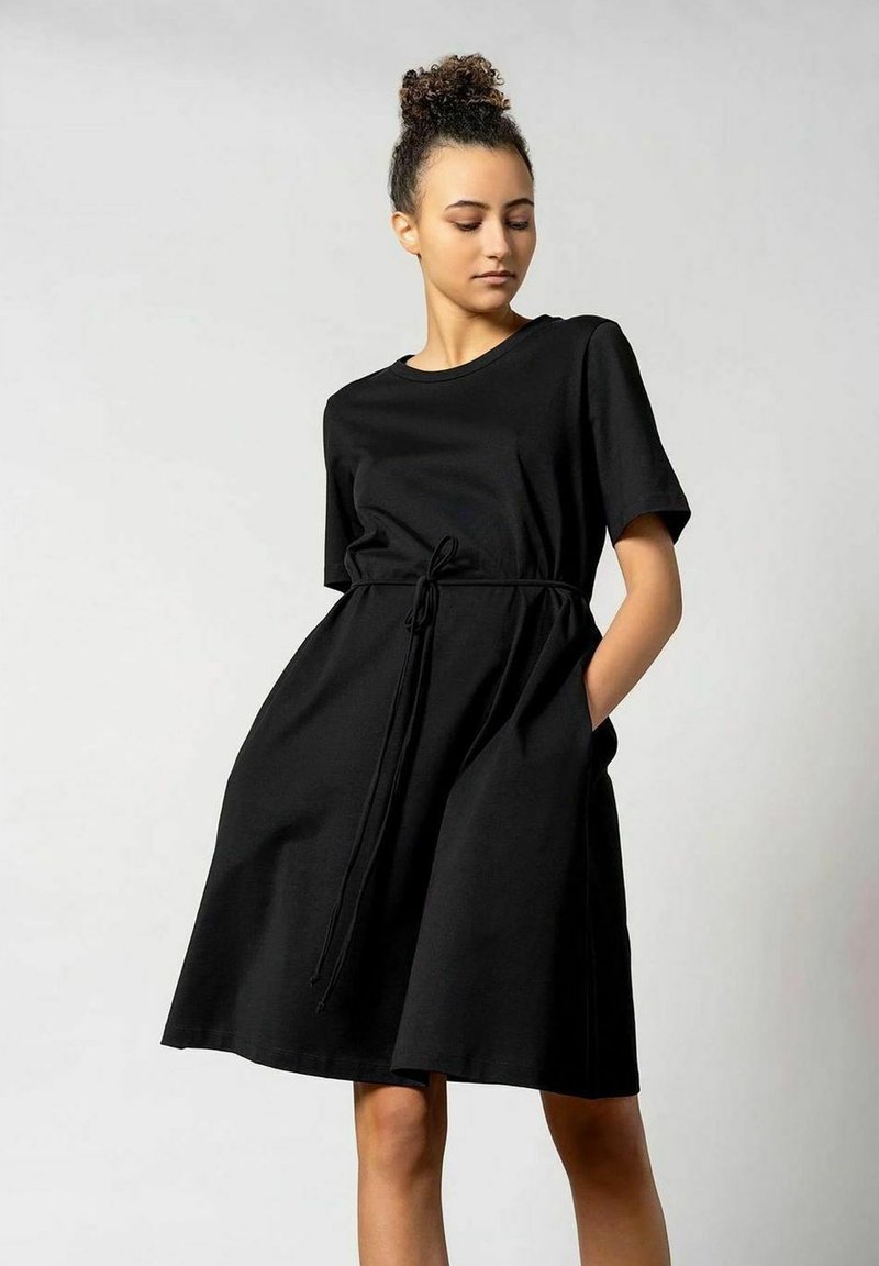 Schwarzes Kurzarmkleid aus weichem Stoff mit lockerer Passform, einem Zugband in der Taille und seitlichen Taschen. Glatte Textur und knielanges Design.