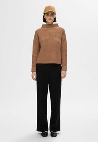 Braun geripptes Sweatshirt mit hohem Kragen, kombiniert mit schwarzen, weit geschnittenen Hosen und einer passenden braunen Mütze. Glatte Textur und lockerer Schnitt.