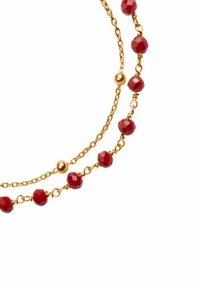 Złoty naszyjnik z łańcuszka z czerwonymi, fasetowanymi koralikami i kulistymi akcentami, prezentujący warstwowy wzór oraz błyszczące wykończenie.