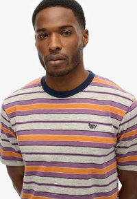 Stribet T-shirt lavet af blødt stof, med vandret striber i lilla, orange og grå, med en marineblå krave og små logo-detaljer.
