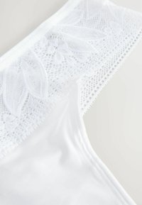 Lingerie blanche avec une bordure en dentelle présentant des motifs floraux, un tissu texturé et une finition lisse. La dentelle a un bord festonné et un design complexe.