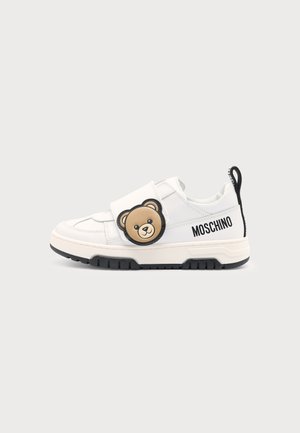 Baskets blanches Moschino avec semelle noire, présentant un visage d'ours en peluche sur la bride et le logo Moschino sur le côté.