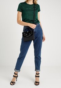 Zielony błyszczący t-shirt o dopasowanym kroju. Niebieskie dżinsy z wysokim stanem. Czarna torebka o strukturalnym kształcie z ozdobnymi akcentami. Czarne sandały na obcasie z paskami.