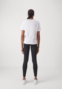 T-shirt branco de manga curta combinado com leggings pretas; tecido suave, corte justo e design simples, complementado por ténis brancos.