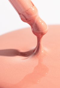 Cosmético líquido en un tono melocotón brillante, con un gotero que dispensa una formulación brillante que refleja la luz, creando una textura suave.