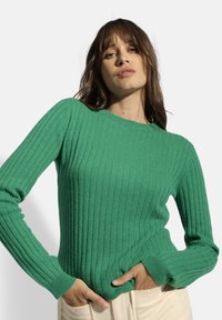 Suéter verde de canalé con mangas largas y cuello redondo, hecho de una tela suave. Diseño texturizado, ajustado y con un ligero elasticidad.