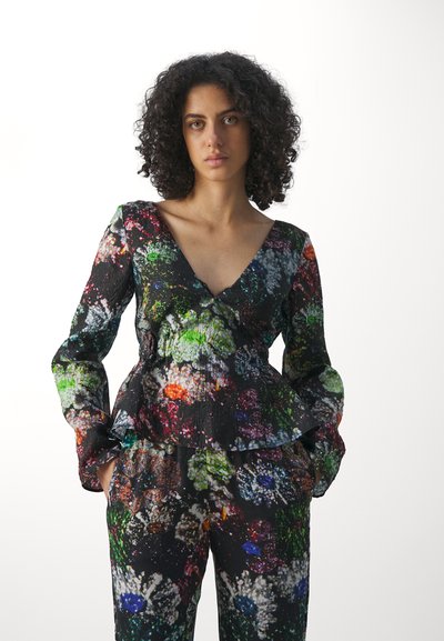 Blouse multicolore à motifs avec un design peplum, manches longues et décolleté en V profond. Caractérisée par un tissu texturé avec des éclaboussures de vert, rouge et bleu.