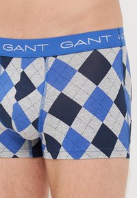 Boxeri scurți cu un model albastru și gri, prezentând un design în diamant, fabricați dintr-un material moale, cu un tiv elastic albastru, branduit "GANT."