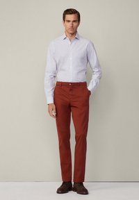 Man in een lichtblauw geruit overhemddesign en roestkleurige broek, gecombineerd met bruine veterschoenen. Eenvoudig ontwerp en slim fit.