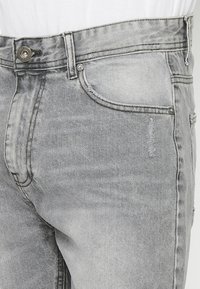 Sivé džínsy z denimu s klasickým piatym vreckovým dizajnom, zapínaním na gombík a jemným vyblednutím látky, s decentným kontrastným stehom.