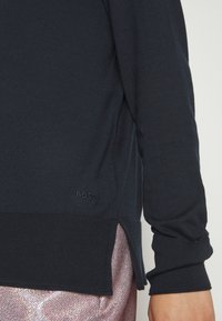 Pull en tricot bleu marine avec poignets et ourlet côtelés. Comprend une fente latérale et un logo "BOSS" brodé en bas à gauche.