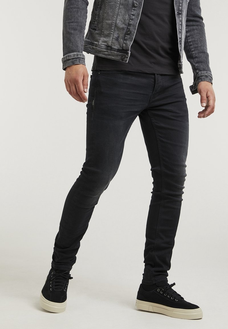 Svarta denim skinny jeans med en blekt finish, kombinerat med en grå denimjacka och svarta sneakers med en strukturerad övre del och vit sula.