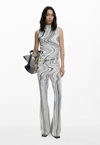 White sleeveless top and matching flared pants featuring a black wavy stripe pattern; accessorized with a multi-colored handbag.