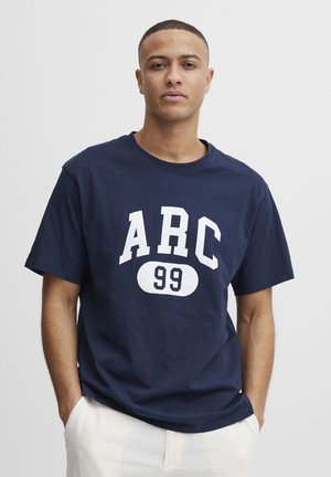 Mørkeblå T-shirt lavet af bomuld, med en iøjnefaldende hvid "ARC 99" grafik på fronten. Rund hals og korte ærmer, løs pasform.