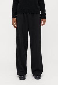 Pantalons larges noirs en tissu lisse, avec une taille haute et un devant plissé. Associés à des chaussures à plateforme noires.