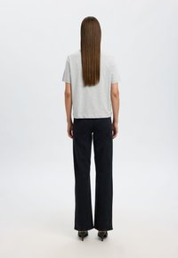 Camiseta de algodón gris de manga corta combinada con unos vaqueros negros de pierna ancha y cintura alta. Cabello largo y liso cae por la espalda.