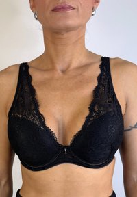 Sujetador negro de encaje con escote pronunciado, que presenta un estampado floral, tirantes ajustables y cierre frontal. Textura suave y detalles intrincados.