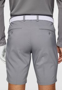 Harmaat golfsortsit, joissa on sileä rakenne, sivutaskut, nappiyksityiskohtia ja valkoinen kootut vyö. Vyötärö istuu mukavasti lantion ylle.