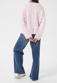 Pull en tricot rose à manches longues et ourlet côtelé, associé à un jean bleu ample et des ballerines beige. La texture douce est visible.