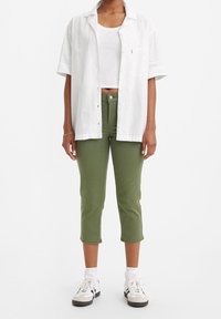 Biała koszula z krótkim rękawem zestawiona z bia łym topem na ramiączkach, w połączeniu z oliwkowymi, dopasowanymi spodniami typu cropped i białymi trampkami.