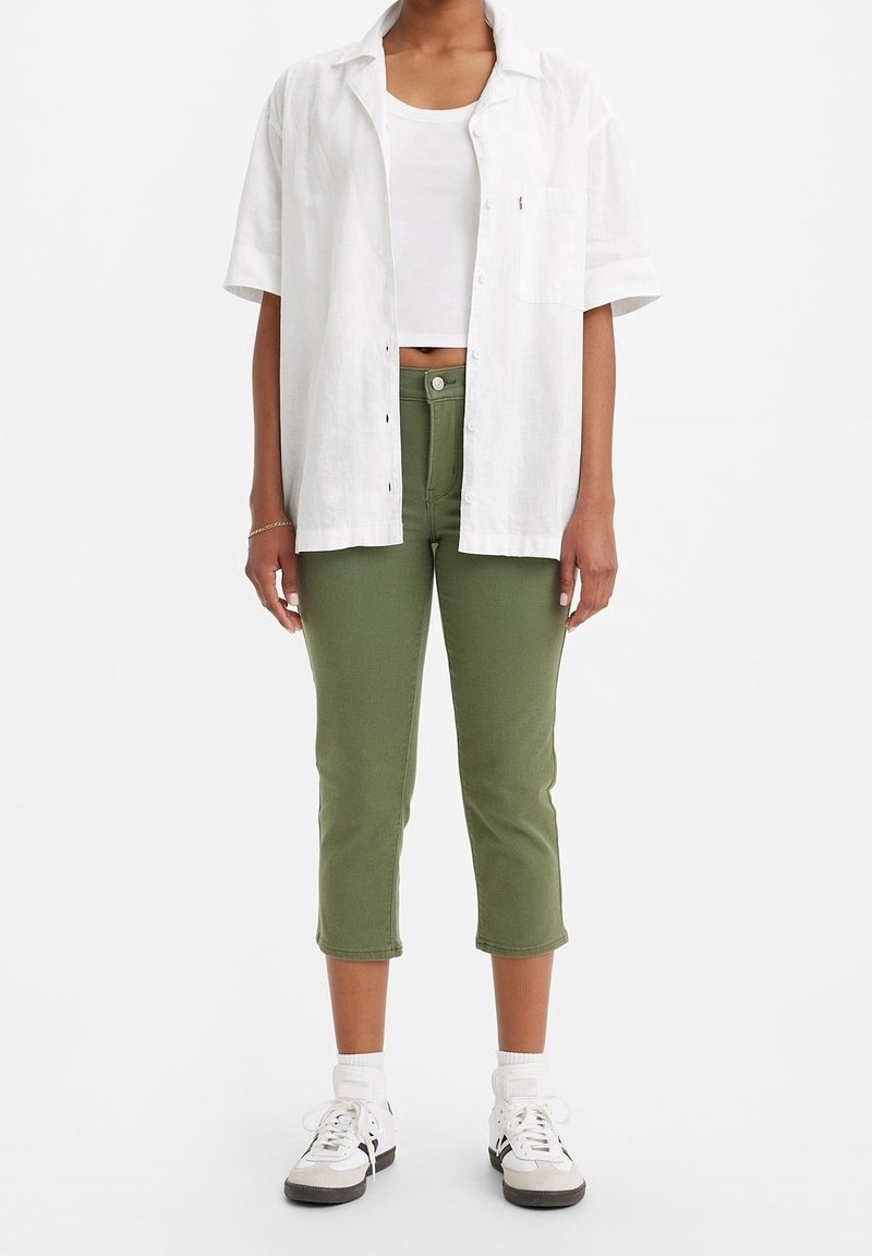 Biała koszula z krótkim rękawem zestawiona z białym topem na ramiączkach, w połączeniu z oliwkowymi, dopasowanymi spodniami typu cropped i białymi trampkami.