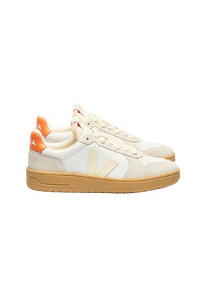 Zapatillas blancas con acentos de ante beige, puntera perforada y suela de goma. Presentan una pestaña en el talón de color naranja y un logo en el lateral.