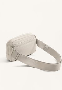 Borsa a tracolla in tessuto beige con scomparto principale con cerniera e tracolla regolabile. Presenta una texture liscia e una forma rettangolare.