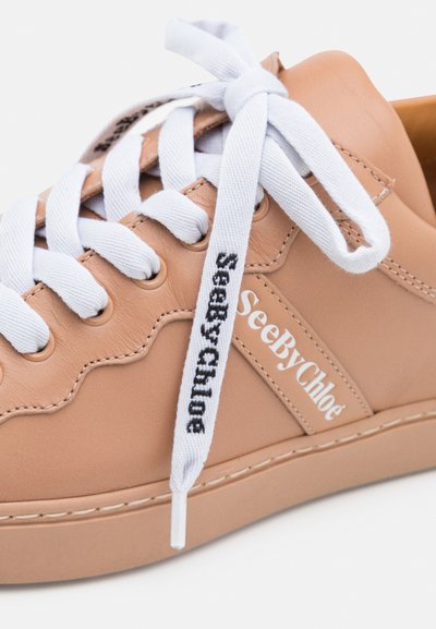 Zapatilla de cuero beige con cordones blancos, con la marca "SeeByChloe" en el lateral. Textura suave y diseño de punta redonda.