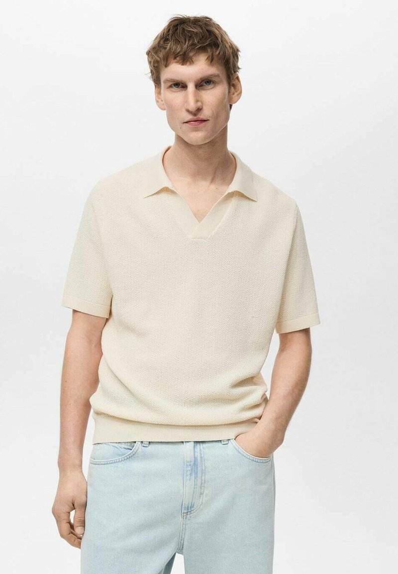 Cream-colored short-sleeve polo shirt with a textured knit, featuring a V-neckline and a relaxed fit, paired with light blue jeans.