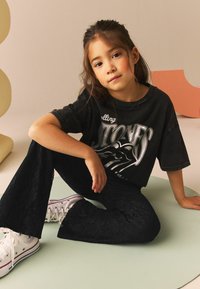 Sort grafisk T-shirt med et Rolling Stones design, parret med sorte flared bukser med blondermønster og hvide sneakers med lilla accenter.