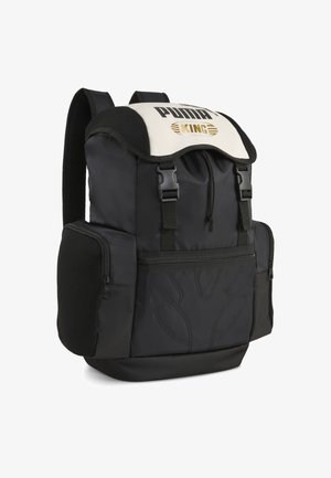 Črn nahrbtnik z belim zgornjim pokrovom, na katerem je v zlati barvi napis "PUMA KING". Vključuje stranske žepe z zadrgami in teksturirane poudarke na trakovih.